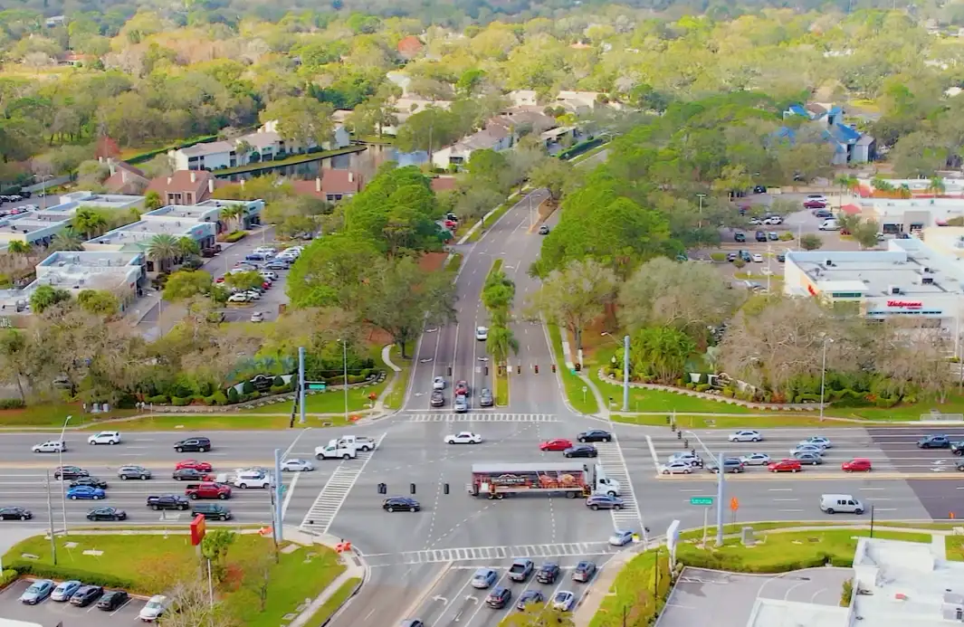 Aerial view of a busy Carrollwood, Florida intersection lined with shopping centers, oak trees, and Bay Area traffic