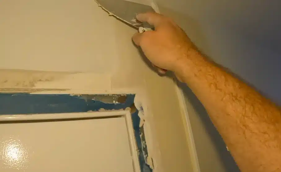 Contractor scraping damaged drywall around a door frame, an important repair step in burst pipe water damage what to do guides