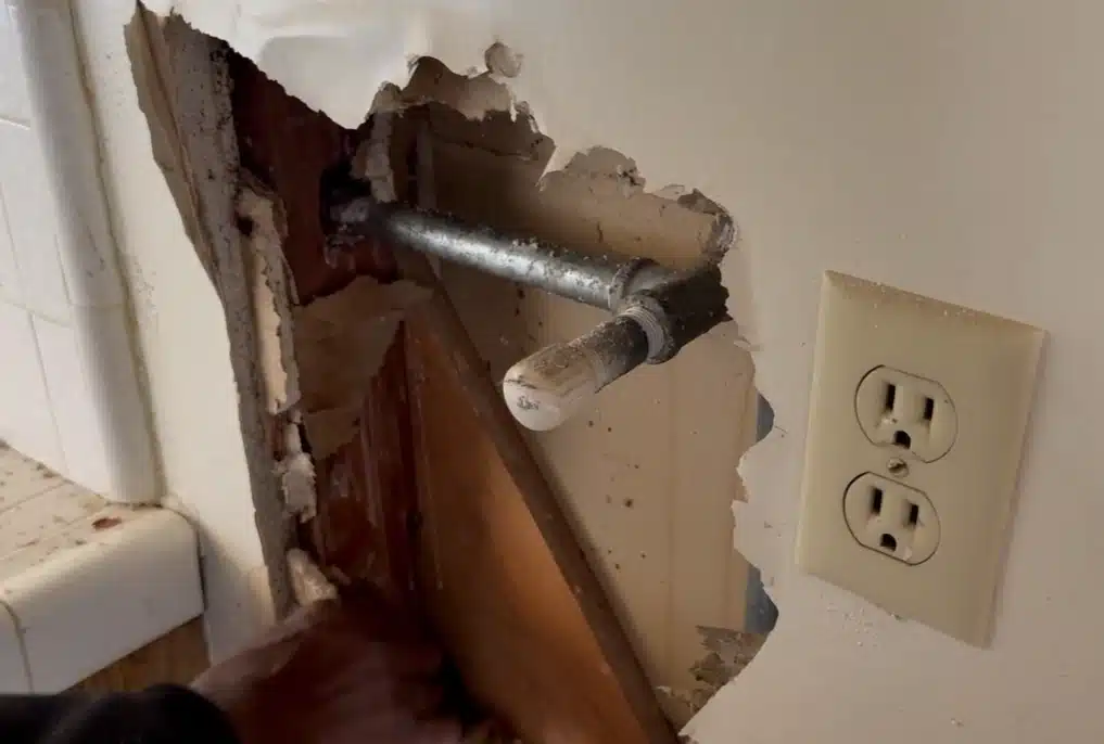 Torn drywall exposing a leaking supply pipe, one of the clearest signs of hidden water damage in walls near electrical outlets